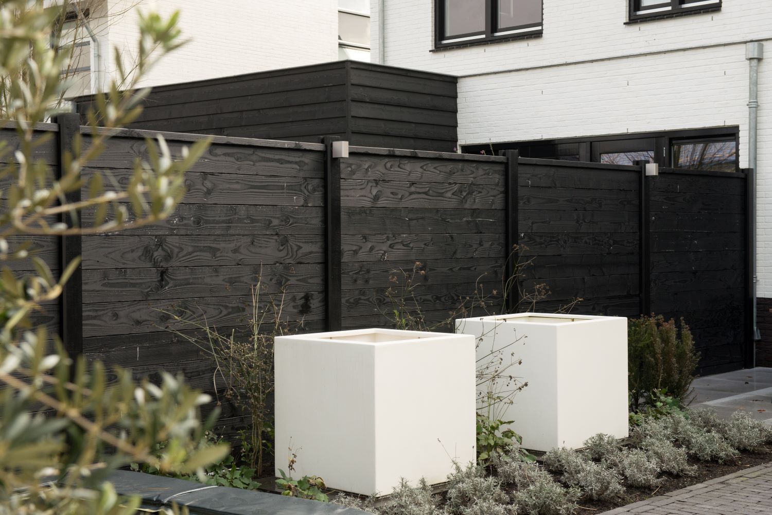 Contrast in een moderne tuin met zwarte schutting en witte bloembakken